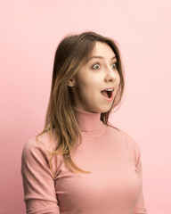 The surprised and astonished young woman screaming with open mouth isolated on pink background. concept of shock face human emotion