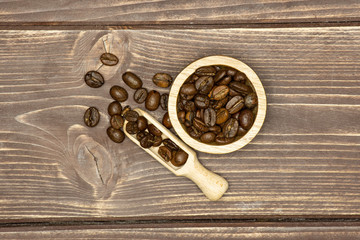 Lot of whole dark brown coffee beans sweet arabica variety in a scoop with wooden bowl flatlay on brown wood