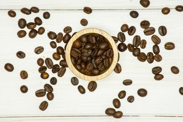 Lot of whole dark brown coffee beans sweet arabica variety with wooden bowl flatlay on white wood
