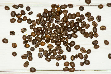 Lot of whole dark brown coffee beans sweet arabica variety flatlay on white wood