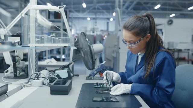 Young Female and Man in Blue and White Work Coats are Using Pliers to Assemble Printed Circuit Boards for Smartphones. Electronics Factory Workers in a High Tech Factory Facility.