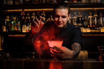 Bartender sprinkling red colored bitter into a cocktail glass