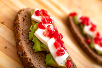 Slice of bread with avocado, cherry tomato, pomegranate seeds and fresh cheese.