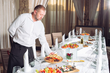 Waiter serving table in the restaurant preparing to receive guests.