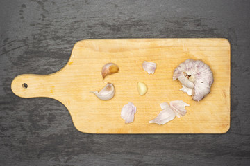 Peeling garlic bulb. recipe step by step farfalle with arugula leaves on chopping board flatlay on grey stone