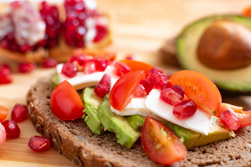 Slice of bread with avocado, cherry tomato, pomegranate seeds and fresh cheese.