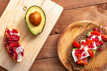 Slice of bread with avocado, cherry tomato, pomegranate seeds and fresh cheese.