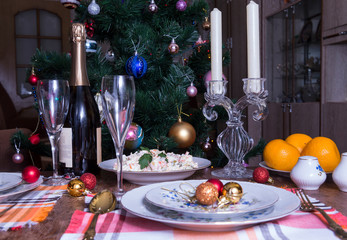 served festive new year's table, plates, salad, glasses, bottle of sparkling wine, candles, Christmas tree in the room, Christmas balls