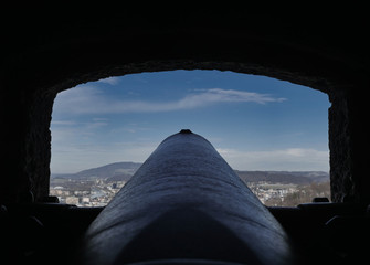 Old cannon at a castle points at city before blue sky