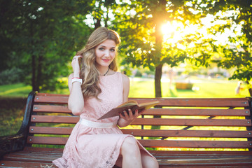 Obraz premium A young girl reading a book sitting on a bench at sunset.
