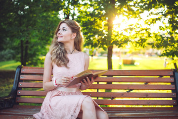 A young girl reading a book sitting on a bench at sunset.