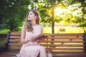 Obraz premium A young girl reading a book sitting on a bench at sunset.