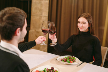 Beautiful young couple with glasses of red wine in luxury restaurant