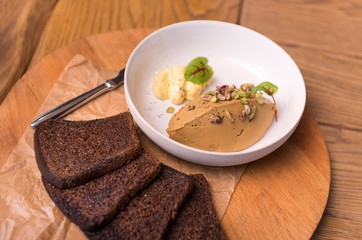 chicken pate with nuts greens and butter on a white plate, toast, toast of rye bread, a knife on a wooden Board for serving, snack on a wooden table
