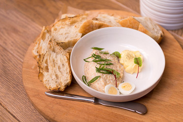 chicken pate on a white plate, pieces of baguette on a wooden Board, knife, snack on the table
