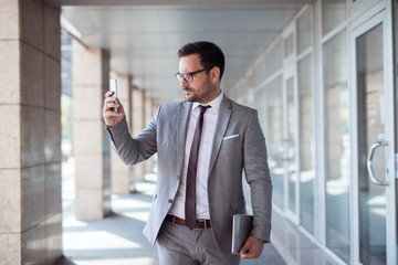 Fototapeta premium Sirious businessman reading text message while walking on the street. In other hand tablet.