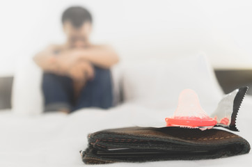  a brown wallet and a pink condom on a white bed. A person is sitting on the bed in the background.