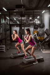 Fototapeta na wymiar Two sporty women stepping up on stepper in gym. Healthy lifestyle concept.