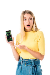 shocked young woman holding smartphone with booking application on screen and looking at camera isolated on white
