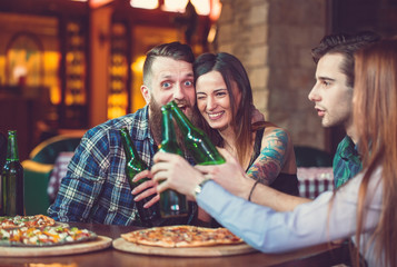 Friends having a drinks in a bar, They are sitting at a wooden table with beers and pizza.