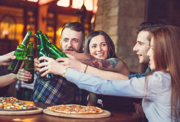 Friends having a drinks in a bar, They are sitting at a wooden table with beers and pizza.