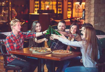 Friends having a drinks in a bar, They are sitting at a wooden table with beers and pizza.