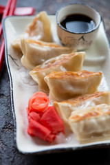 Close-up of a white plate with japanese gyoza, dipping sauce and ginger, vertical shot