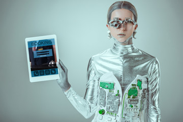 silver robot holding tablet with booking appliance isolated on grey, future technology concept