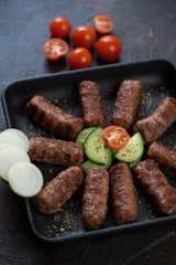 Barbecued balkan cevapi or skinless beef sausages with vegetables and onion, selective focus, closeup