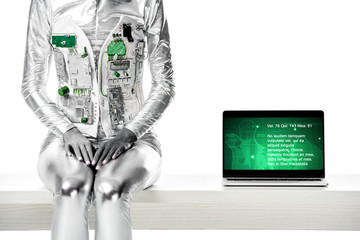 cropped image of robot sitting on table near laptop with medical appliance isolated on white, future technology concept