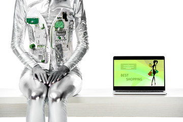 cropped image of robot sitting on table near laptop with best shopping appliance isolated on white, future technology concept