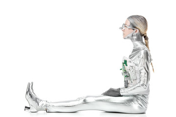 side view of silver robot sitting and looking away isolated on white, future technology concept