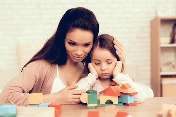 Woman and Sad Child Collect Cubes on Table at Home