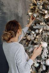 A young brunette woman is dressing up a Christmas tree at home. Stylish Christmas interior.