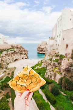 Italy, Puglia, Polognano a Mare, woman's hand holding piece of zucchini focaccia