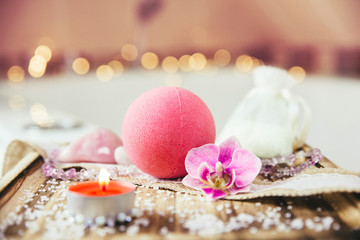 Pink bath ball with orchid flower, scented candle and bath salt on wooden tray in bath room. Therapy concept. Taking a relaxing bath.