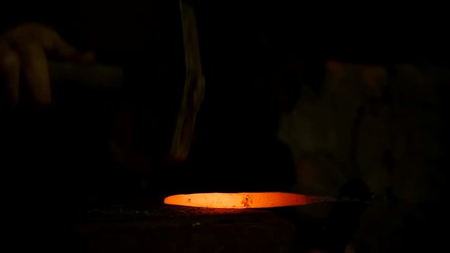 blacksmith works metal. Craftsman, the Highlander on private smithy in the village. Hot rod puts on the anvil, the master hits him with a sledgehammer. On the blacksmith's forge lies a sledgehammer