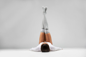 Over head view of a beautiful brunette fitness model wearing tight,  gray fitness shorts with long gray socks and a white long sleeve sports top laying on the ground with feet up and crossed in studio