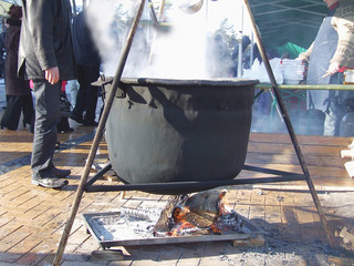 Boiling hot iron pot hanging over open fire. Water vapor coming up from the pot. Cooking or city...
