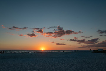 sunset over the sea at fort myers beach, sun touching the water, small clouds in red light hue