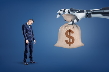 A large robotic hand gives a big money bag with a dollar sign to a small sad businessman.