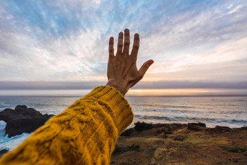 Person hand reaching out to sky on seashore