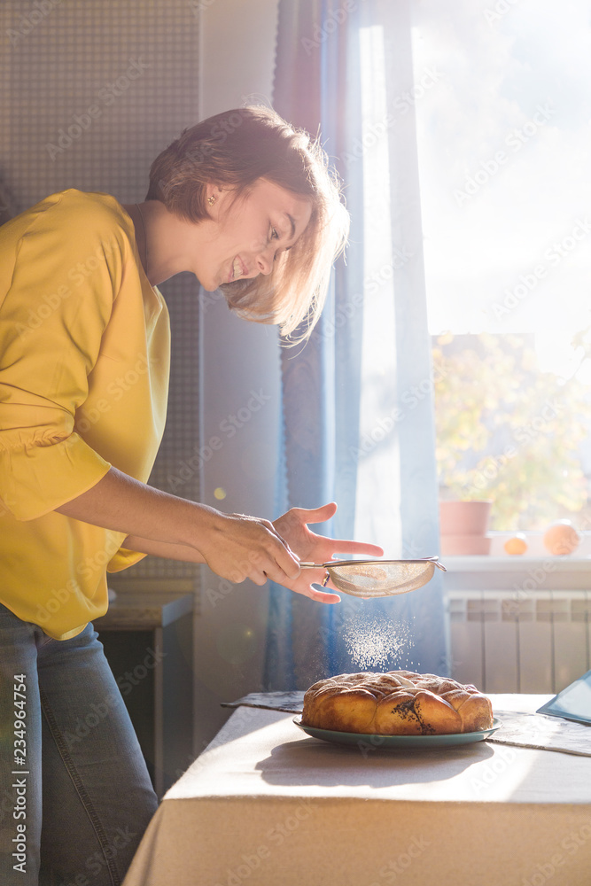 Wall mural pretty smiling girl sprinkle the pie with powdered sugar. homemade food