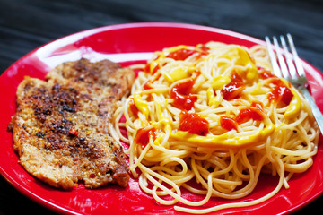 Closeup of grilled steak with pasta and tomatoes on red plate on dark wooden background