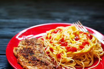 Closeup of grilled steak with pasta and tomatoes on red plate on dark wooden background