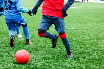 Young Active sport heathy boys in red and blue sportswear running and kicking a red ball on football field with artificial turf. soccer youth team plays football. activities for kids, training