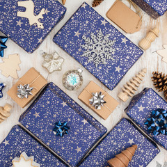 Creative chritmas composition. Presents in dark blue wrapping paper with silver stars and sparkles, wooden decorations, ornaments, paper tags on white table, overhead view, selective focus