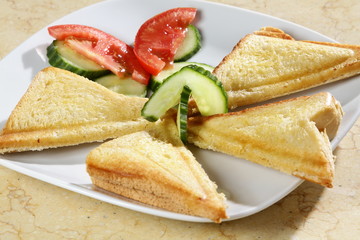 A shot of three triangle sandwiches with tomatoe and cucumber on the side