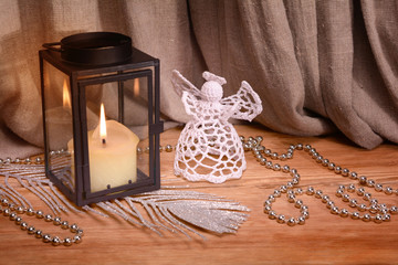 Christmas decoration on wooden background. White crochet angel, lantern, candle, silver feather and beads
