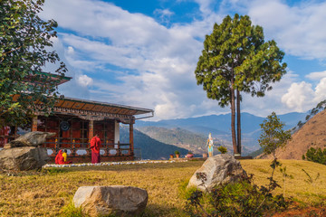 young women monks of the Buddhist monastery in their traditional red robes before classes next to the prayer wheel against the background of the Himalayan mountains